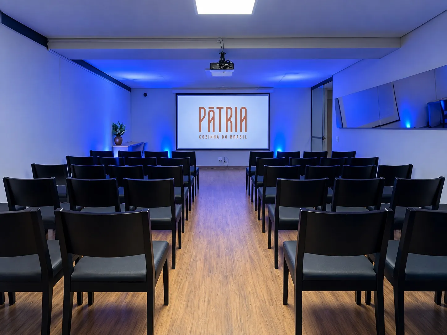 Auditório com cadeiras pretas e projeção do logo do Pátria sob luz azul